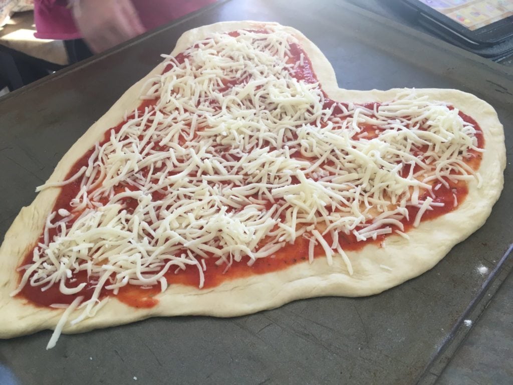 sprinkling cheese on heart shaped pizza